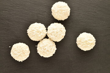 Obraz na płótnie Canvas Several round white candies with coconut flakes on a slate board, close-up, top view.