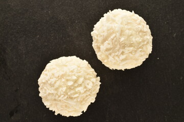 Two round white candies with coconut flakes on a slate board, close-up, top view.