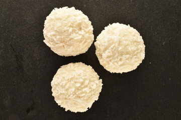 Obraz na płótnie Canvas Three round white candies with coconut flakes on a slate board, close-up, top view.