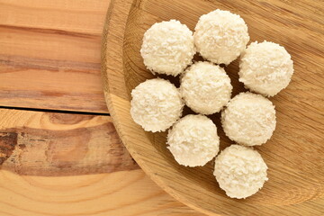 Three delicious sweets with coconut flakes with a wooden plate on a wooden table, close-up, top view.