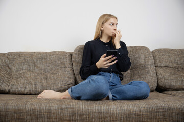 Thoughtful young caucasian girl on couch with modern phone work on content blogging looking to aside
