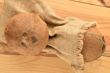 Two ripe organic coconuts with a jute bag on a wooden table, close-up, top view.