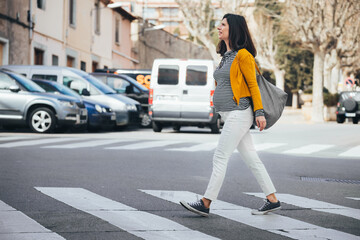Brunet caucasian pregnant woman walking on the streets of an old city and crossing a crosswalk. Fashionable woman wearing casual clothes going to work. Maternity Lifestyle.