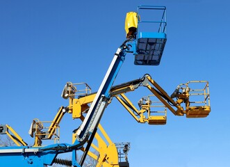 Blue and yellow aerial work platform against clear blue sky