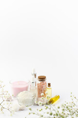 Obraz na płótnie Canvas Spa and wellness concept. Set of natural cosmetic products such as serums, oils, cosmetic clay, aromatic candles and beautiful flowers on white background. Vertical image. Skin care concept.