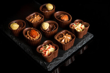 Candy with cream and nuts on a slate board. Assorted chocolate on black isolated background. Idea for dessert in a restaurant