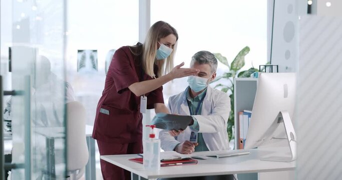 Quarantine. Two medical staff workers in surgical masks discussing x-ray photograph diagnosis analyzing symptoms negotiating in muulti-ethnic office. Hospitals.
