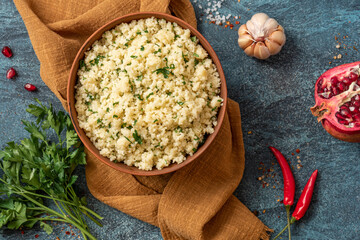 Cooked couscous with parsley in a ceramic bowl on a dark background top view. Maghreb cuisine,...