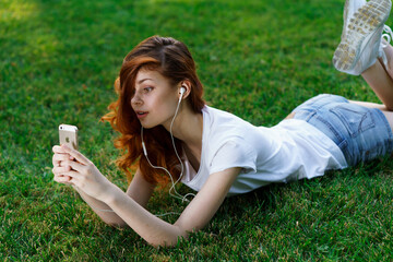 pretty woman lies on the lawn outdoors in the park rest phone in hands