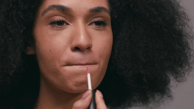 close up view of young african american woman applying lip balm isolated on grey