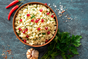 Cooked couscous with parsley and pomegranate in a ceramic bowl on a dark background top view. Maghreb cuisine, vegan food. 