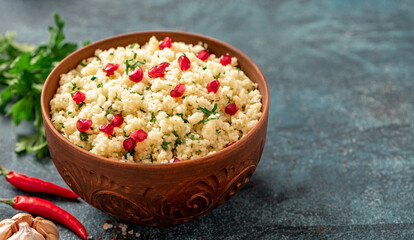 Cooked couscous with parsley and pomegranate in a ceramic bowl on a dark background close-up. Maghreb cuisine, vegan food. Copy space for text