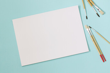 empty blank white paper sheet with paint brushes on the mint green background, mockup for arts