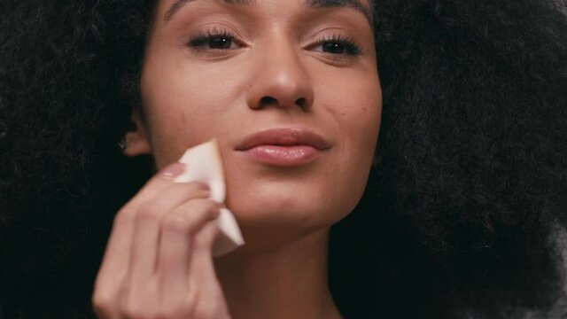 young african american woman applying makeup foundation isolated on grey