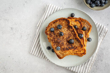 Flat lay of three slices of french toast with blueberries on a plate on grey background, copy space on the left