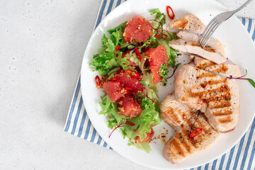 Grilled turkey steaks and lettuce salad with grapefruit in a plate on a white concrete table top view. Healthy diet food. Tasty lunch with turkey meat.