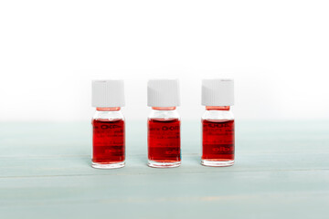 Three medicine vials filled with red liquid arranged in a row on white background