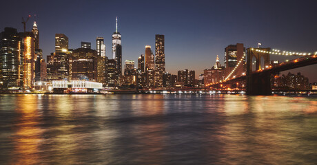 Fototapeta na wymiar Manhattan skyline and Brooklyn Bridge reflected in water at dusk, New York City, USA.