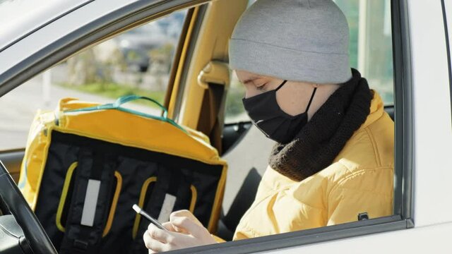 Courier in the car is on his phone, backpack for orders on the seat. Food delivery service