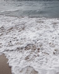 Vertical photo of amazing beach with foamy waves. Indian ocean and sand on Bali island.