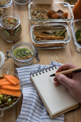 Closeup view of a man hand writing a recipe surrounded of many glass jars full of delicious food.