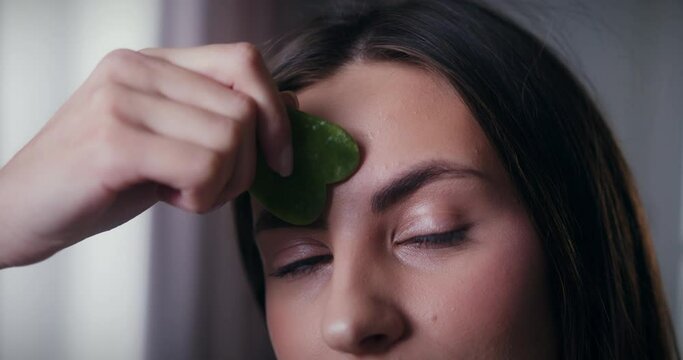 Close-up shot of young beautiful woman massaging forehead with crystal quartz stone to reduce wrinkles. Face lift skincare and beauty rituals concept.