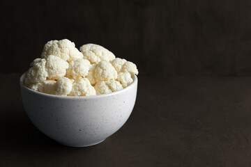 Raw cauliflower slices in a light bowl on a dark background with copy space.