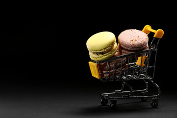 Colorful almond cookies macarons or macaroons in shopping cart on black background. minimalism,...