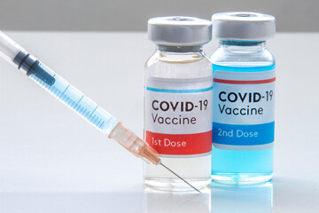 1st dosis and a 2nd dosis of covid-19 vaccine on a vial bottle and injection Syringe on a white table