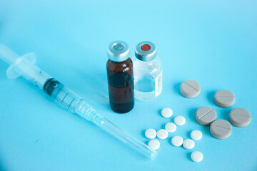 Close up of medical ampoule, syringe and pills isolated on blue background