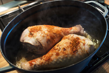 marinated and spiced turkey leg with various vegetables in the casserolle, cooking on the stove.