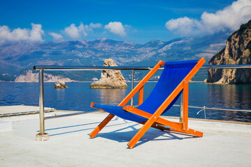View over the board of a boat on sea and grey rock islands with sun loungers