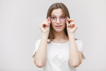 smiling frowning office girl staring at camera through eyeglasses on white background. Young woman adjusting eyewear. Glasses wearing concept