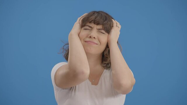 Woman in white shirt against a blue background hits her head for her mistakes.Woman with regret.