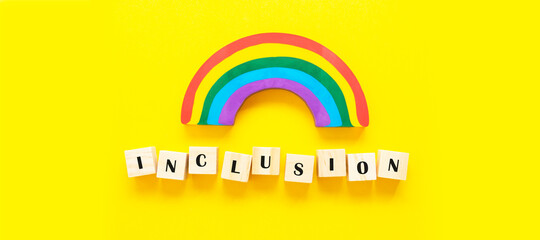 Inclusion concept word on wooden cubes and rainbow on yellow background, banner