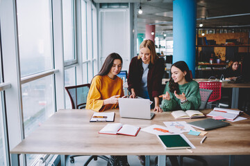 Cheerful female colleagues working on laptop together in cafe
