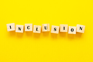 Inclusion concept word on wooden cubes on yellow background