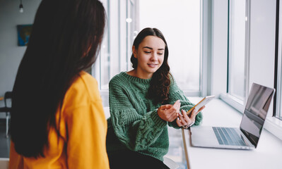 Glad woman explaining strategy to colleague while working with gadgets