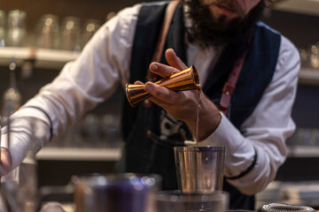 Bartender pouring fresh alcoholic drink into the glasses with ice cubes on the bar counter