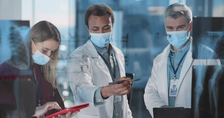 Multi-ethnic team of doctors wearing face masks cooperating in medical office hospital corporate workspace together. - Powered by Adobe