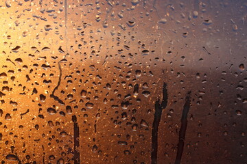 Natural background of condensation of water on a window glass with high air humidity, large drops dripping. Natural sunlight through glass. High humidity