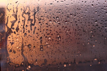 Natural background of condensation of water on a window glass with high air humidity, large drops dripping. Natural sunlight through glass. High humidity