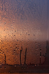 Window transparent glass with condensation, high humidity in the room, large drops of water flow down, warm tone, natural drops