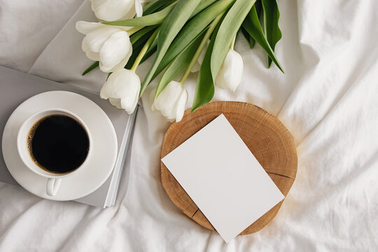 Coffee, white tulips and empty paper card on the bed