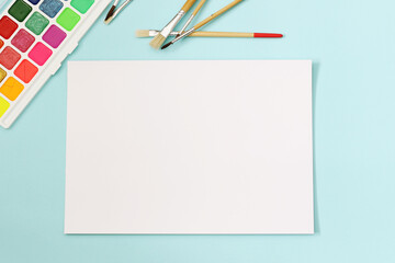 blank white sheet of paper with colourful water colours and painting brushes