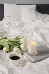 Coffee, candle and white tulips on bed.
