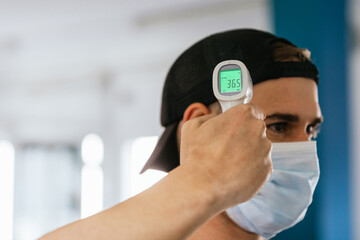 Man with mask taking his temperature. Infrared thermometer. Healthy gym. Pandemic, coronavirus. Concept of health and safety.