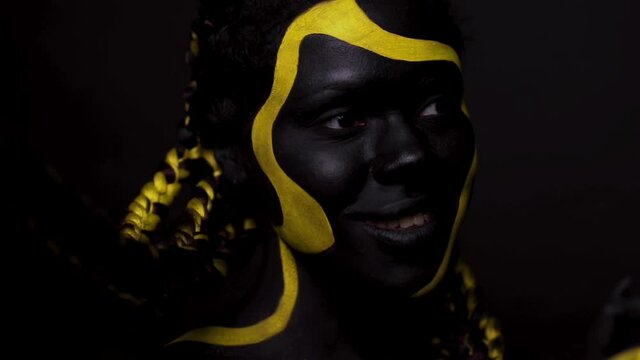 Face art. Dancing woman with black and yellow body paint. Young african girl with colorful bodypaint. An amazing afro american model with yellow makeup. Closeup face.