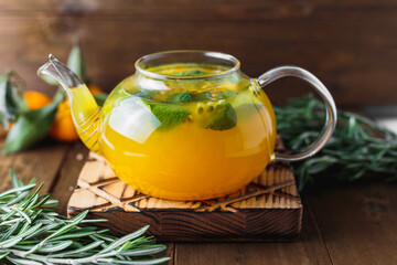 Hot tea with passionfruit and mint in a glass teapot, rosemary and miniature tangerines on the...