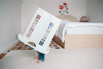 Cute funny baby toddler child with large clothes bin on head. Lonely autistic kid playing alone at...